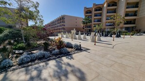 Une cour avec un chemin pavé, entourée de diverses plantes et arbres, et un immeuble à plusieurs étages avec des balcons en arrière-plan.