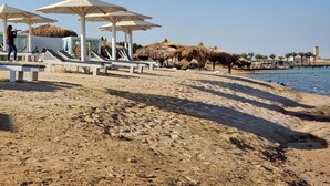Une plage avec des chaises longues et des parasols, une structure à toit de chaume et une vue dégagée sur la mer.
