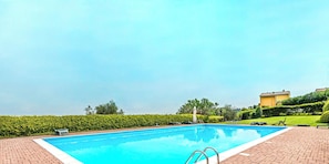 Ein rechteckiger Pool mit klar blauem Wasser, umgeben von einer Ziegelterrasse mit Liegestühlen und einer kleinen weißen Statue.