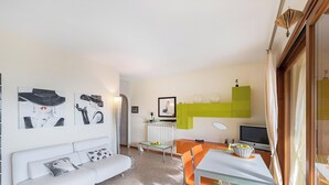 A modern living room with a white sofa, a dining table with orange chairs, and artwork on the walls. - Poggio Picedo P1 32 by Wonderful Italy (Polpenazze del Garda)