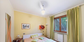 A bedroom with a bed, a window with curtains, a radiator, and a wall-mounted shelf.