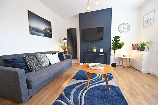 A modern living room with a grey sofa, a round wooden coffee table, and a blue patterned rug.