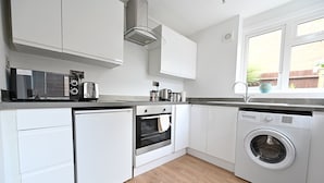 A modern kitchen with white cabinets, a built-in oven, a microwave, a toaster, and a washing machine.