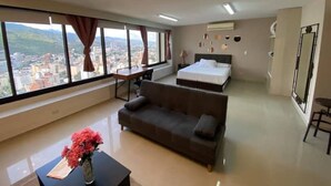 Een moderne hotelkamer met een groot bed, een bank, een bureau en een stadszicht door grote ramen.
