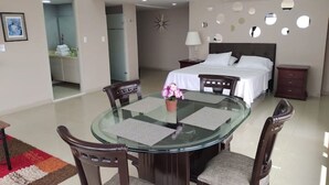 Una camera d'albergo moderna con un tavolo da pranzo in vetro, quattro sedie, un letto con lenzuola bianche, un comodino e una parete con specchi circolari.
