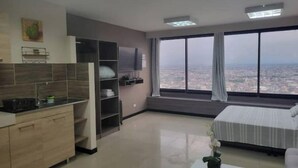 Quarto de hotel moderno com cozinha, uma janela grande e vista para a cidade, e uma cama com vista.