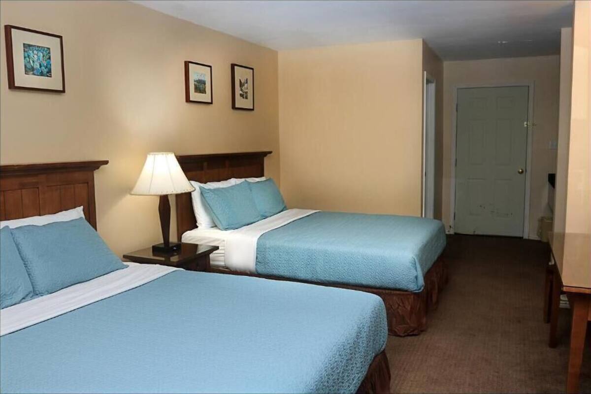 A hotel room with two beds, a nightstand with a lamp, and a door.