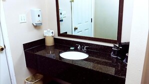 Ein Badezimmer mit Marmorplatte, einem weißen Waschbecken, einem Spiegel, einer Seifenspender und einem Mülleimer.
