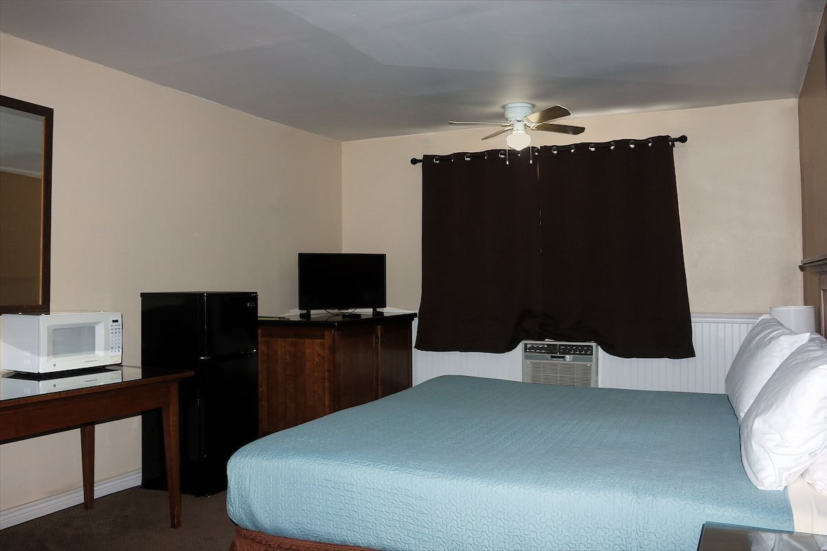 A hotel room with a bed, a desk with a microwave, a television, and a ceiling fan.