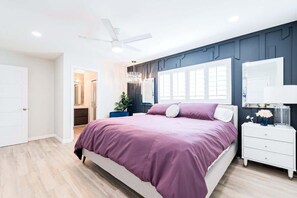 Ein Schlafzimmer mit Bett, Nachttisch, Spiegel, Deckenventilator und einer Tür.