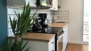 A modern kitchen with white cabinets, a black countertop, a microwave, and a coffee maker. There is a potted plant on the counter.