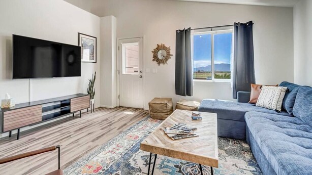 A modern living room with a flat-screen TV, a sofa, a coffee table, and a view of the outdoors through a window.