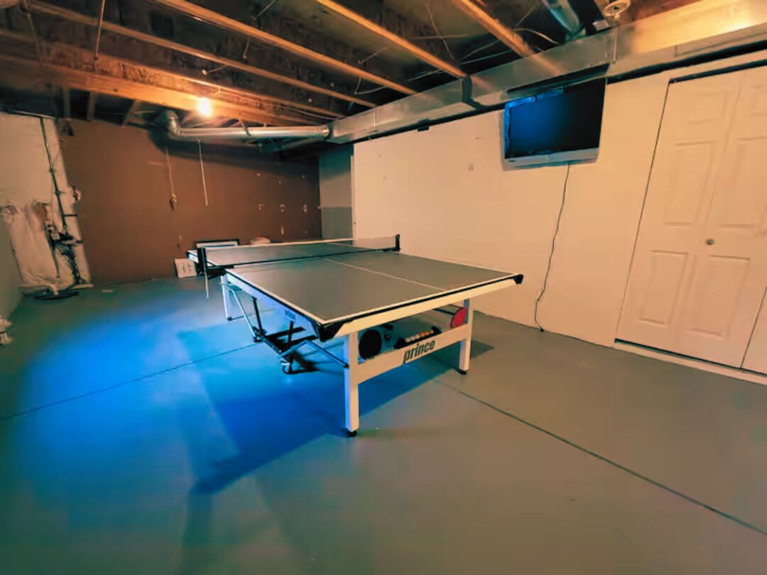 A ping pong table in a room with a white door, a window, and exposed ceiling beams.
