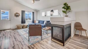 A spacious living room with a fireplace, a sofa, a coffee table, and a large window with a view.