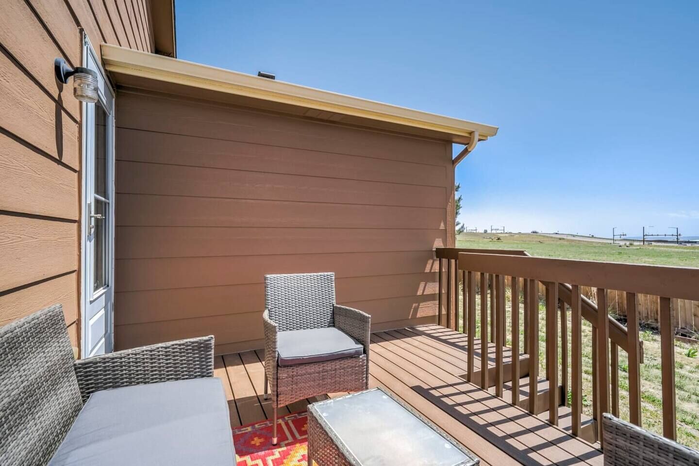 A covered outdoor deck with wicker furniture and a view of a grassy field.