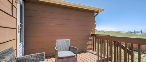 A covered outdoor deck with wicker furniture and a view of a grassy field.