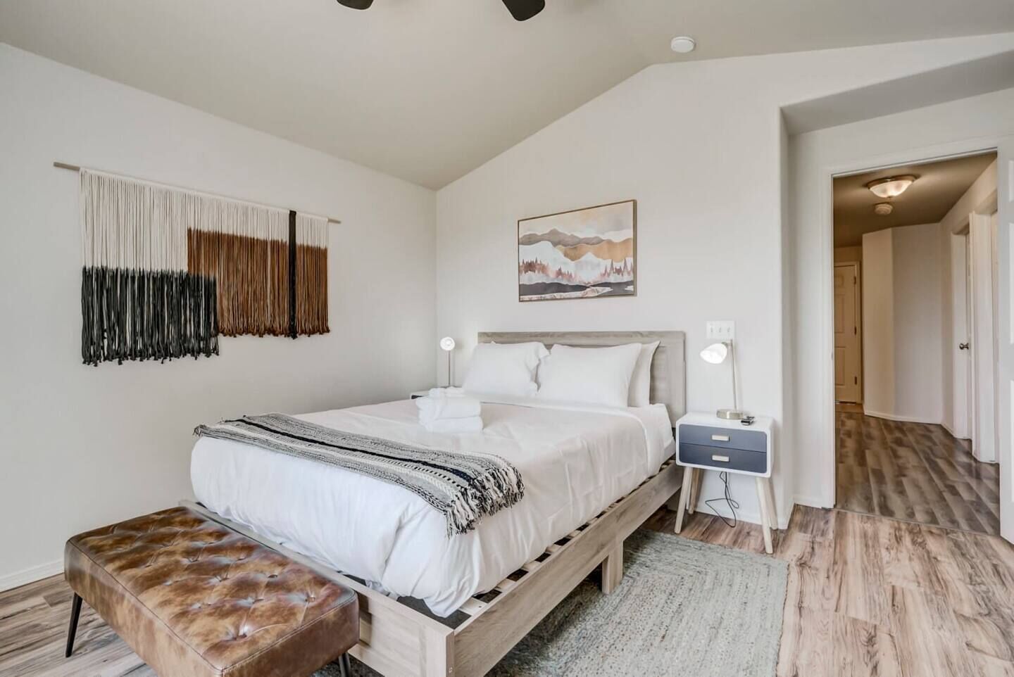 Una camera da letto con un letto di legno, una panca, un comodino con una lampada e un'opera d'arte appesa al muro.