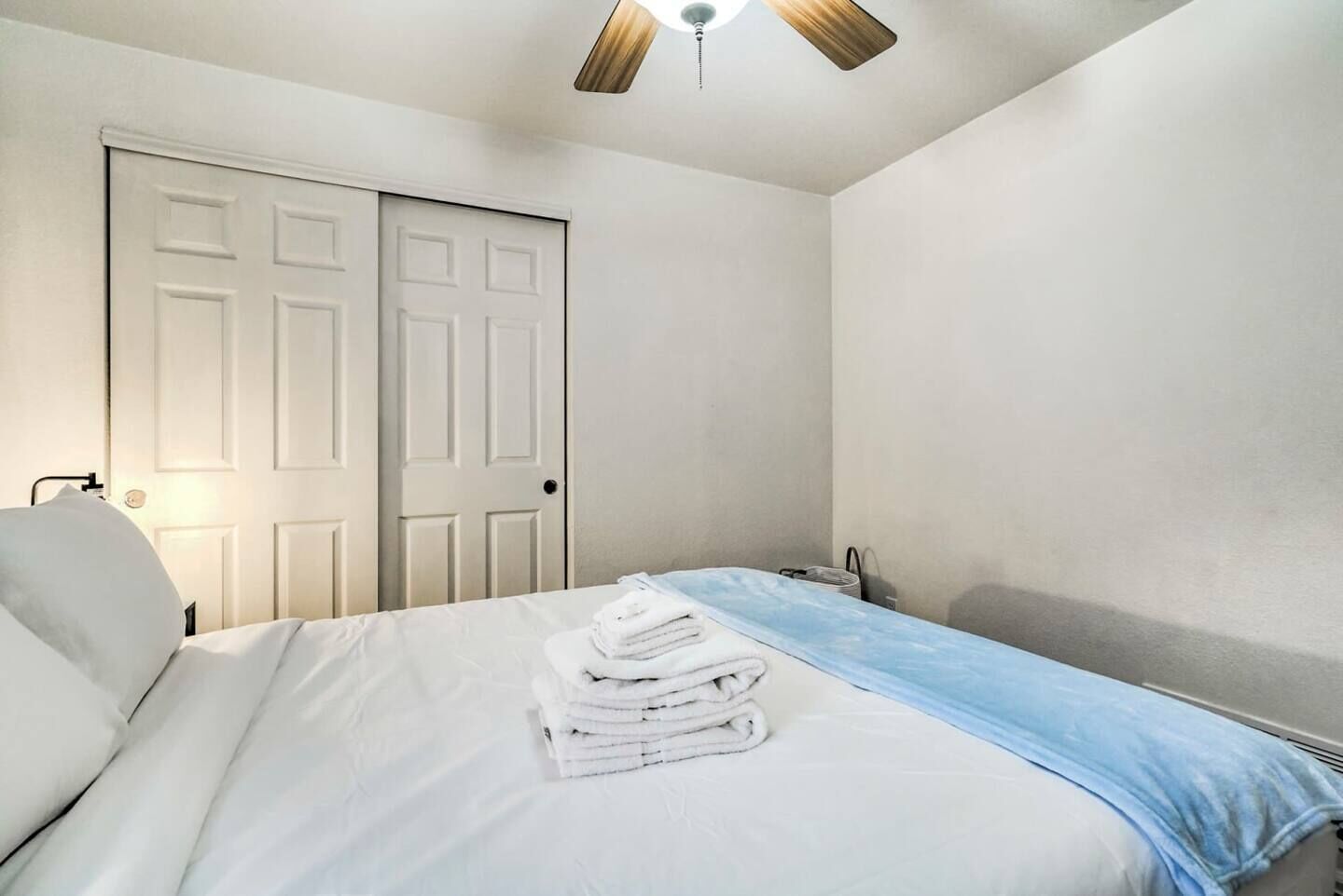 A bedroom with a bed, a stack of white towels, a ceiling fan, and a white door.