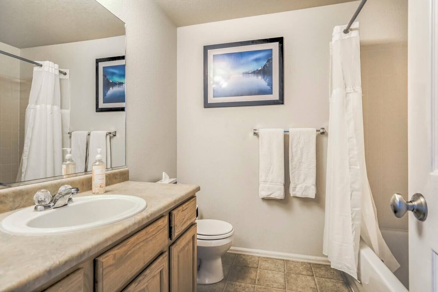 A bathroom with a sink, mirror, toilet, and shower curtain.