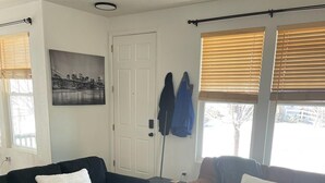 A living room with two sofas, a coffee table, and a door. There is a coat rack with jackets and a painting on the wall.
