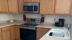 A kitchen with wooden cabinets, a stainless steel microwave, a stove, and a coffee maker.