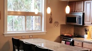 Une cuisine dotée d’une grande fenêtre, d’une cuisinière, d’un four à micro-ondes et de luminaires suspendus.