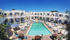 A hotel courtyard with a central pool, outdoor seating, and a multi-story building with balconies. - HOTEL DAR TAOUFIK (Djerba Midun)