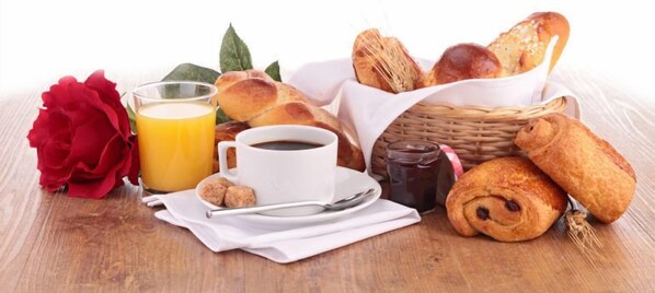 A breakfast setting with bread, a croissant, a glass of orange juice, a cup of coffee, and a red flower.