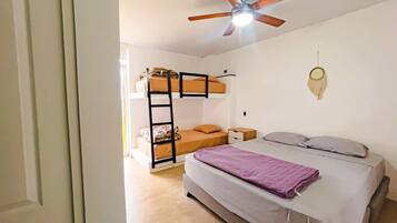 Ein Schlafsaalzimmer mit Etagenbetten, einem Bett, einem Deckenventilator und einem Traumfänger an der Wand.