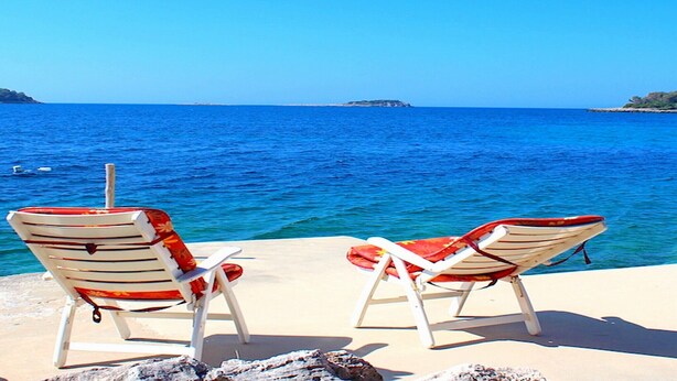 Two beach chairs facing the sea with a clear view of the ocean and a distant island.