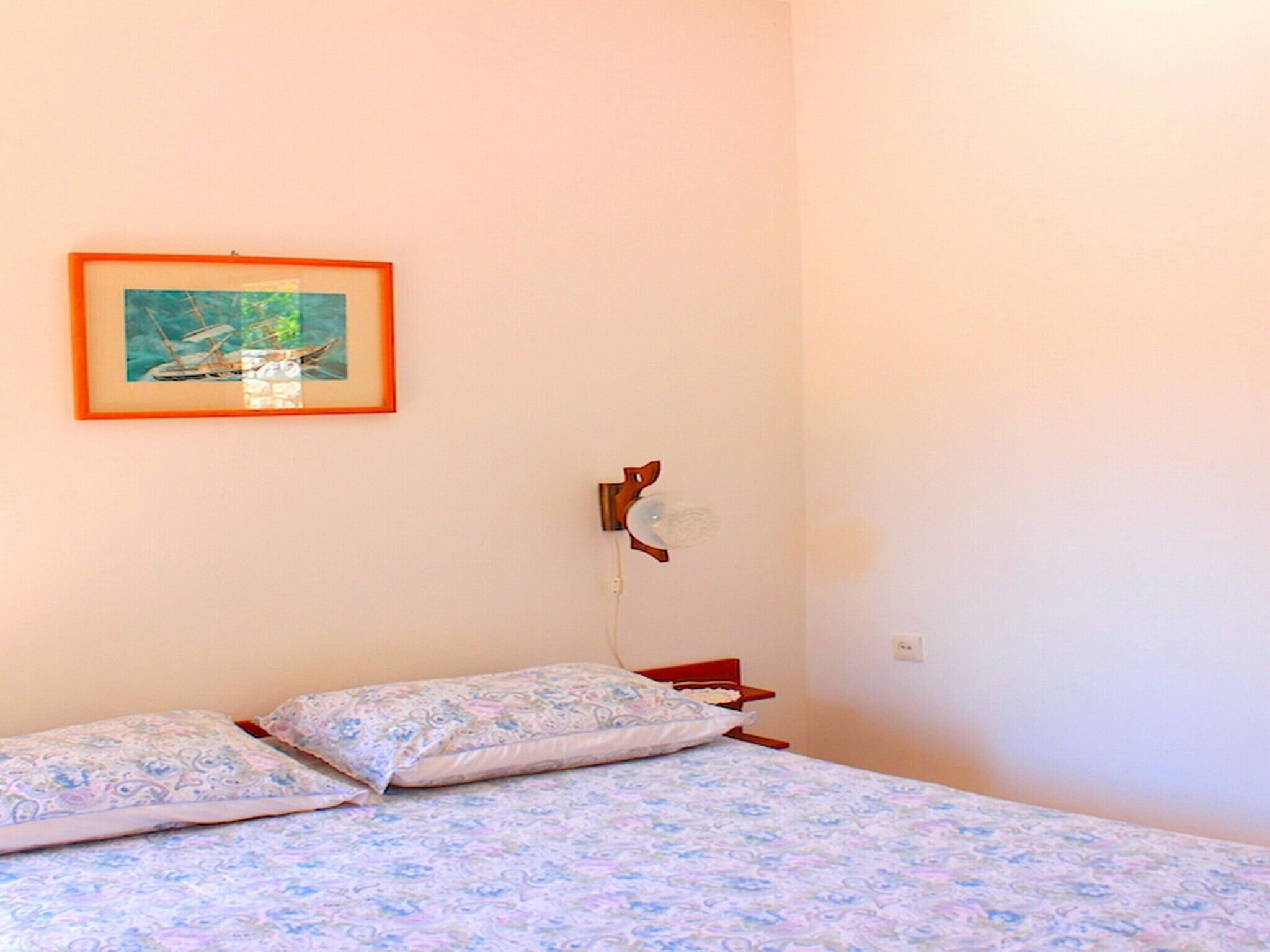 Un dormitorio con una cama, dos almohadas, un cuadro en la pared y un enchufe.