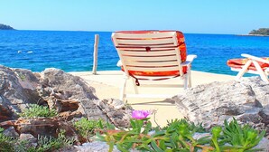 A beach chair with a floral pattern facing the sea, a small flower in the foreground, and rocky terrain.