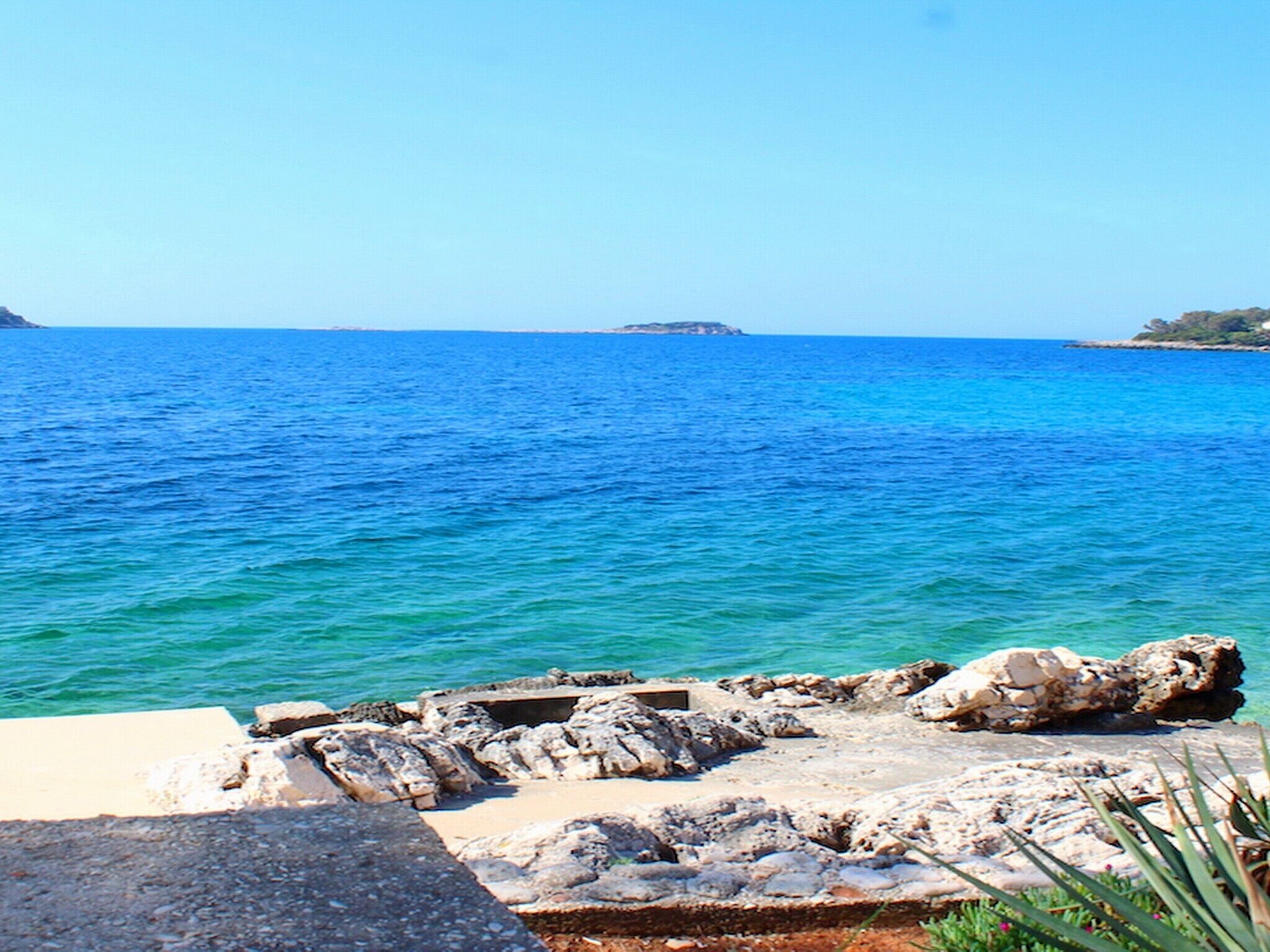 A rocky shoreline with clear blue sea and distant land.
