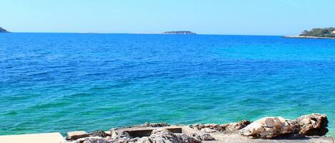 A rocky shoreline with clear blue sea and distant land.