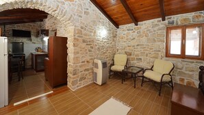 A rustic stone-walled room with a wooden ceiling, a kitchen area with a stove, and two chairs. - Stone House Lozica Vela Luka (Vela Luka)