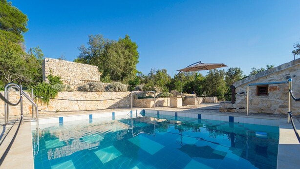 A clear blue swimming pool with stone walls and a stone building in the background. - Stone House Lozica Vela Luka (Vela Luka)