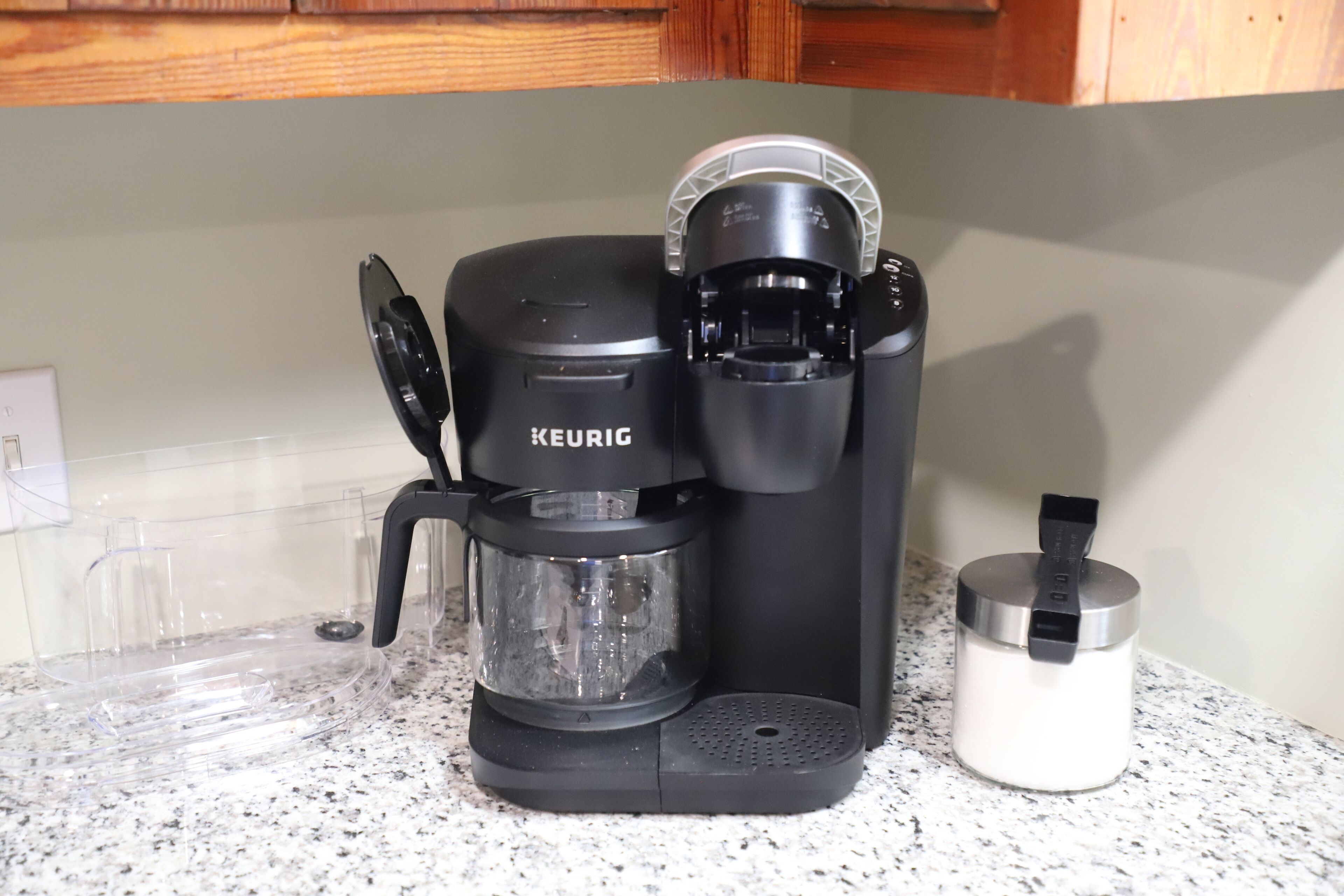 Eine Kaffeemaschine von Keurig auf einer Küchenarbeitsplatte mit einer klaren Glascarafe und einer weißen Tasse.