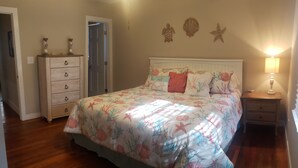 A bedroom with a floral bedspread, a wooden dresser, a nightstand with a lamp, and a door leading to another room. - 6 Bed/4 Bath whole house duplex, minutes from golf, restaurants, and the beach! (Murrells Inlet)