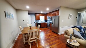 A modern kitchen with wooden cabinets, a stainless steel refrigerator, and a dining area with a wooden table and chairs. - 6 Bed/4 Bath whole house duplex, minutes from golf, restaurants, and the beach! (Murrells Inlet)