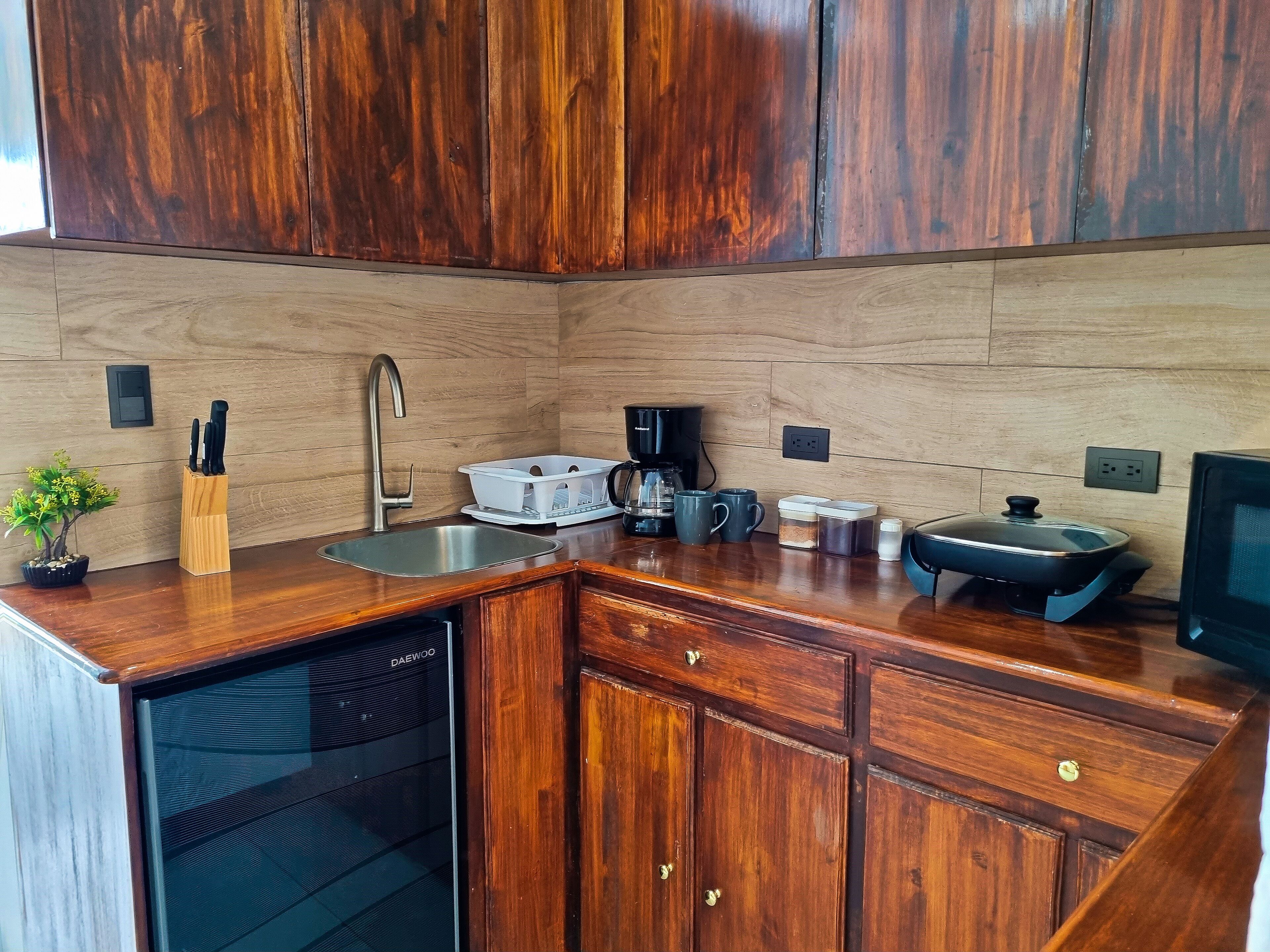 A compact kitchen with wooden cabinets, a stainless steel sink, a coffee maker, and a built-in dishwasher.