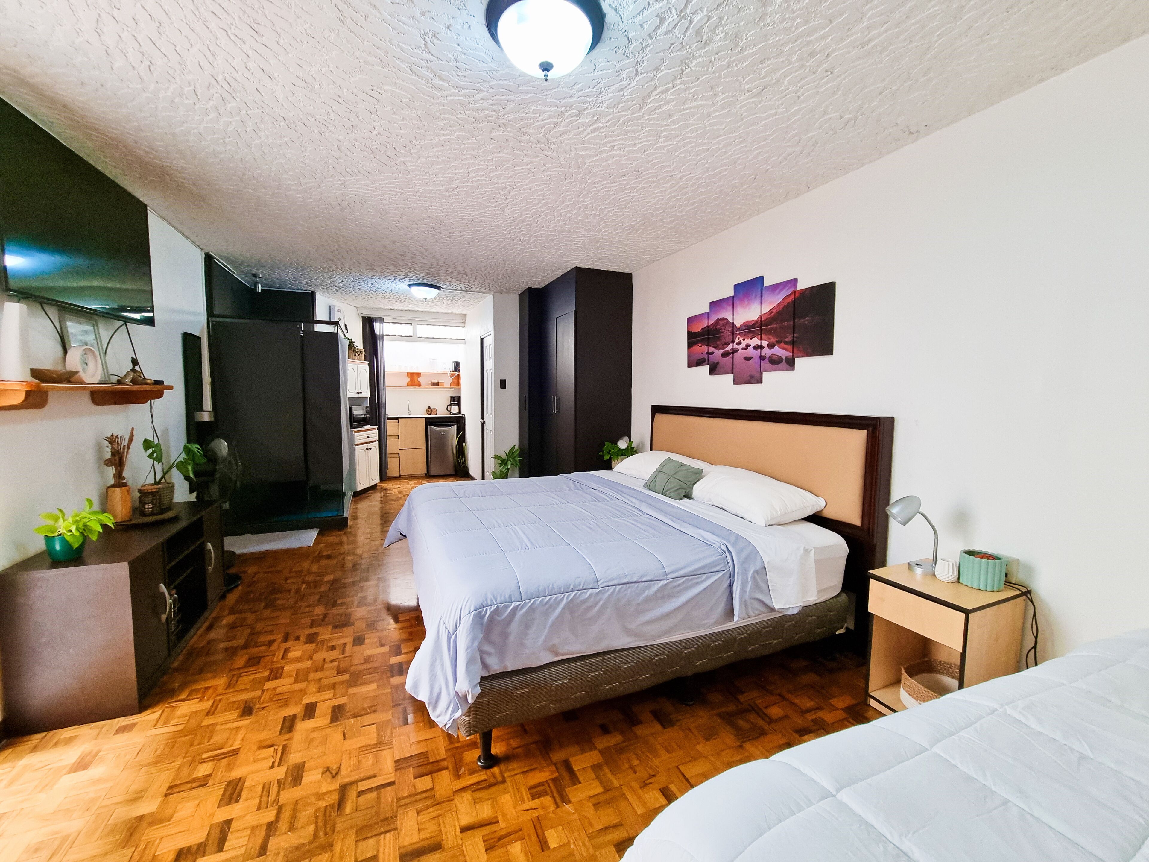 A bedroom with a bed, bedside table, and a view into the kitchen.