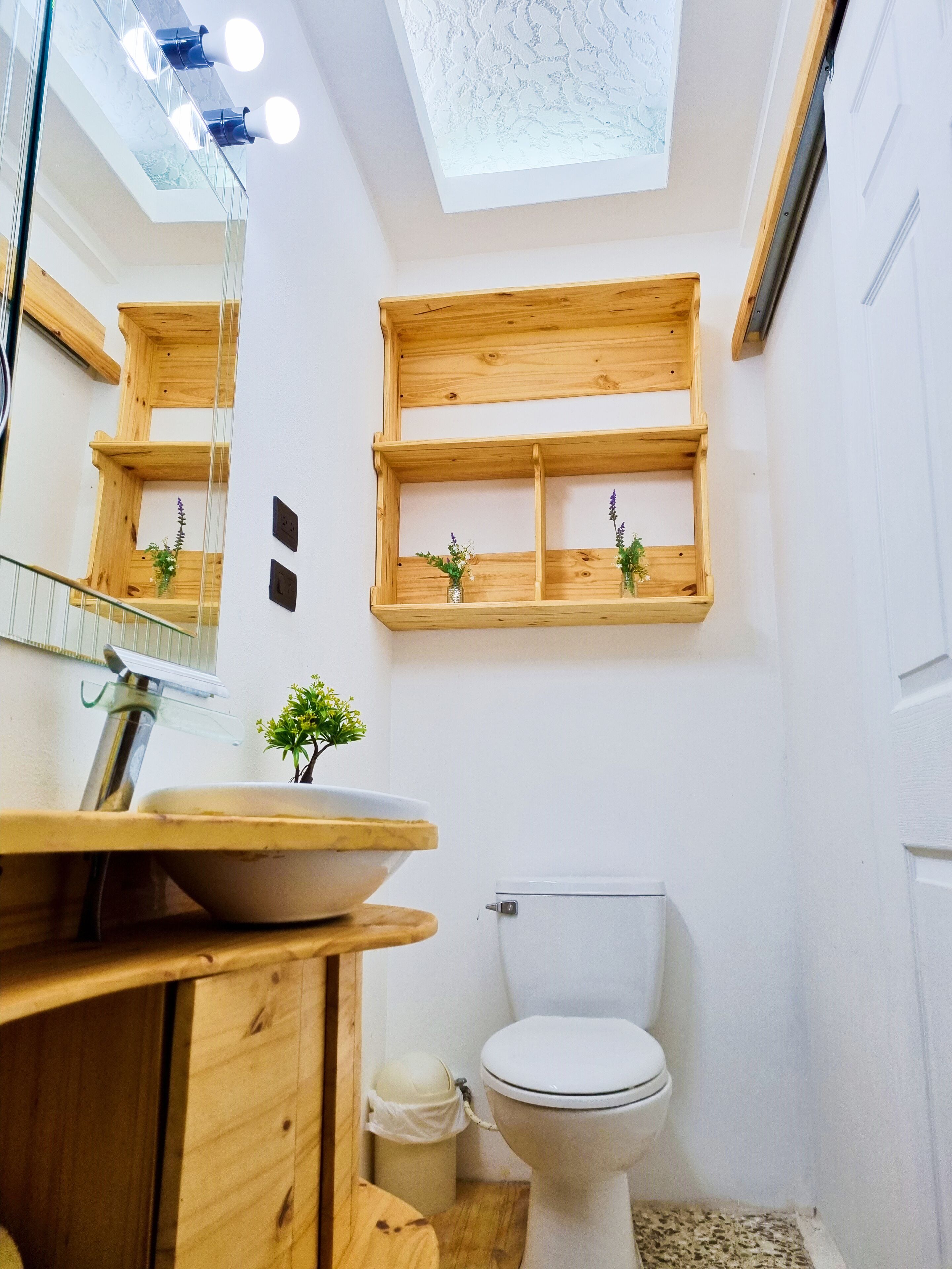 Une salle de bain avec un meuble-lavabo en bois, des toilettes blanches et des étagères en bois ornées de plantes.