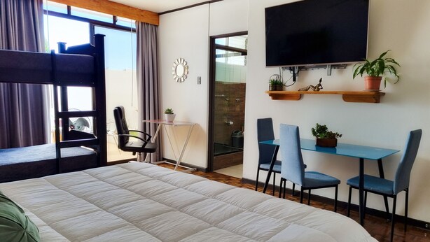 A hotel room with a large bed, a desk with two chairs, a TV, and a balcony with a view.