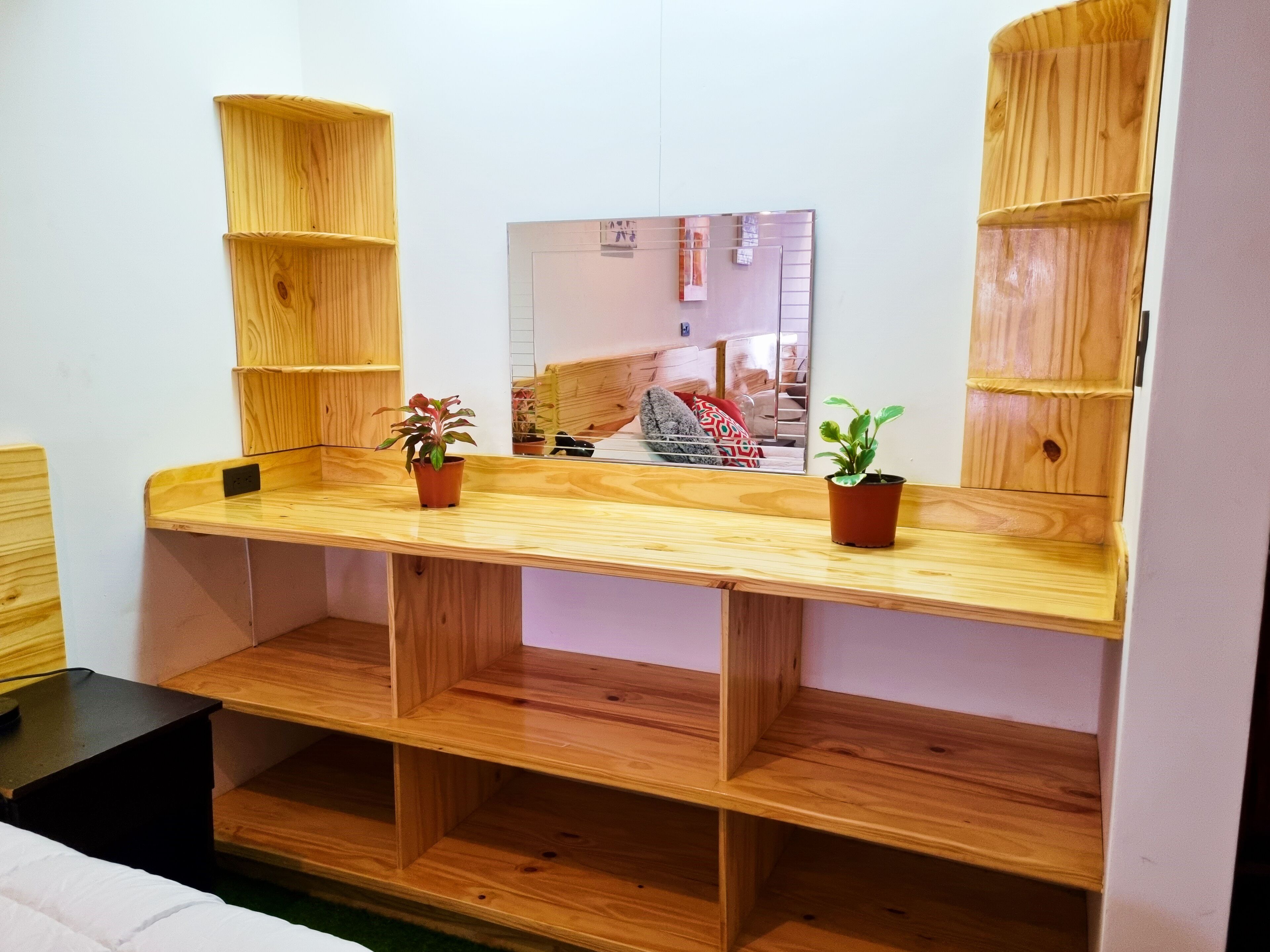 Un escritorio de madera con dos macetas, un espejo y estantes empotrados.