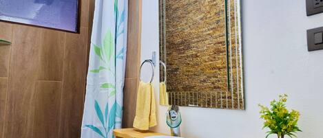 A bathroom with a wooden vanity, a white sink, a mirror, a shower curtain with a leaf pattern, a towel rack, and a small potted plant.