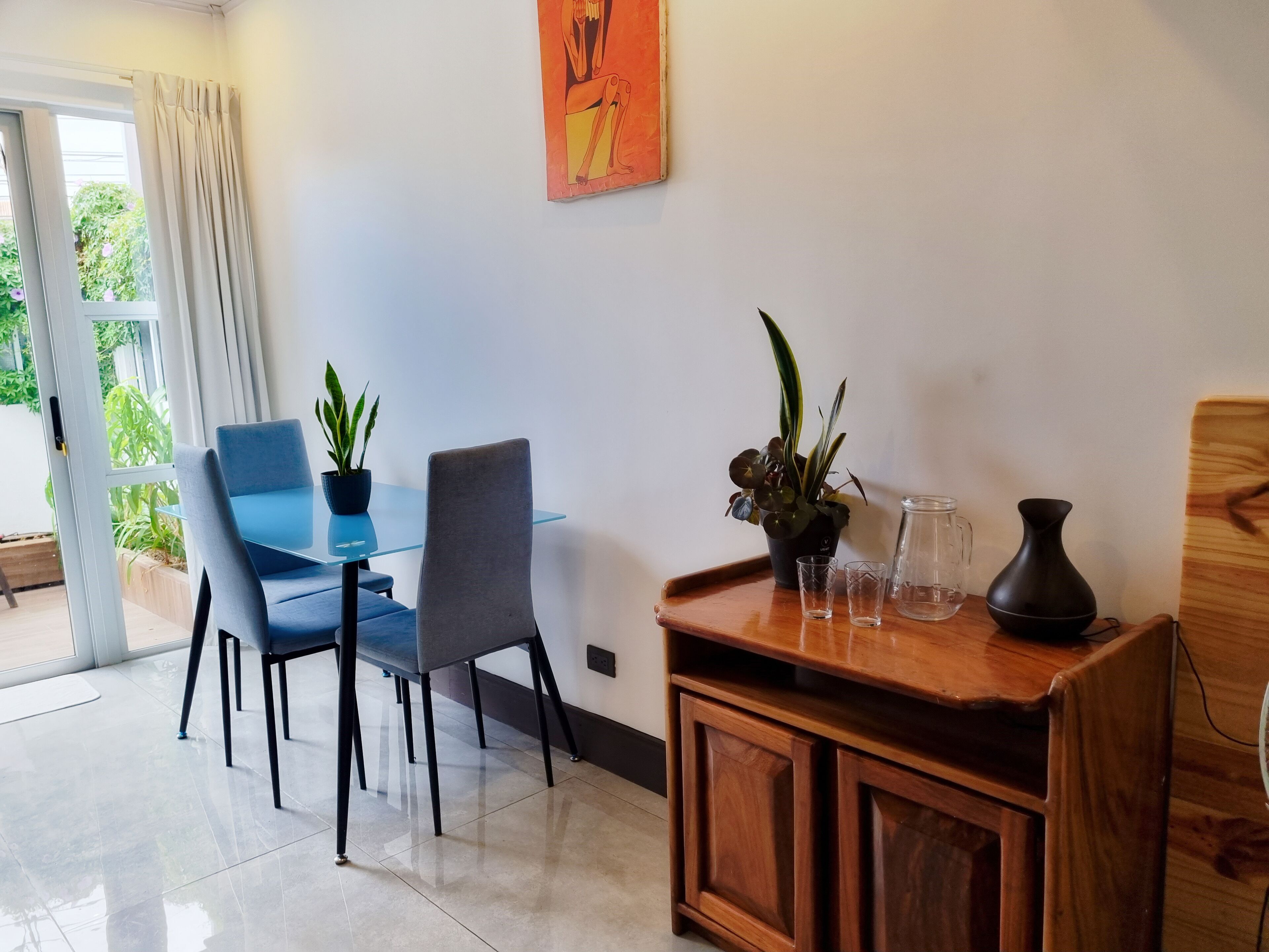 A modern dining area with a glass table, two chairs, and a wooden cabinet with decorative items.