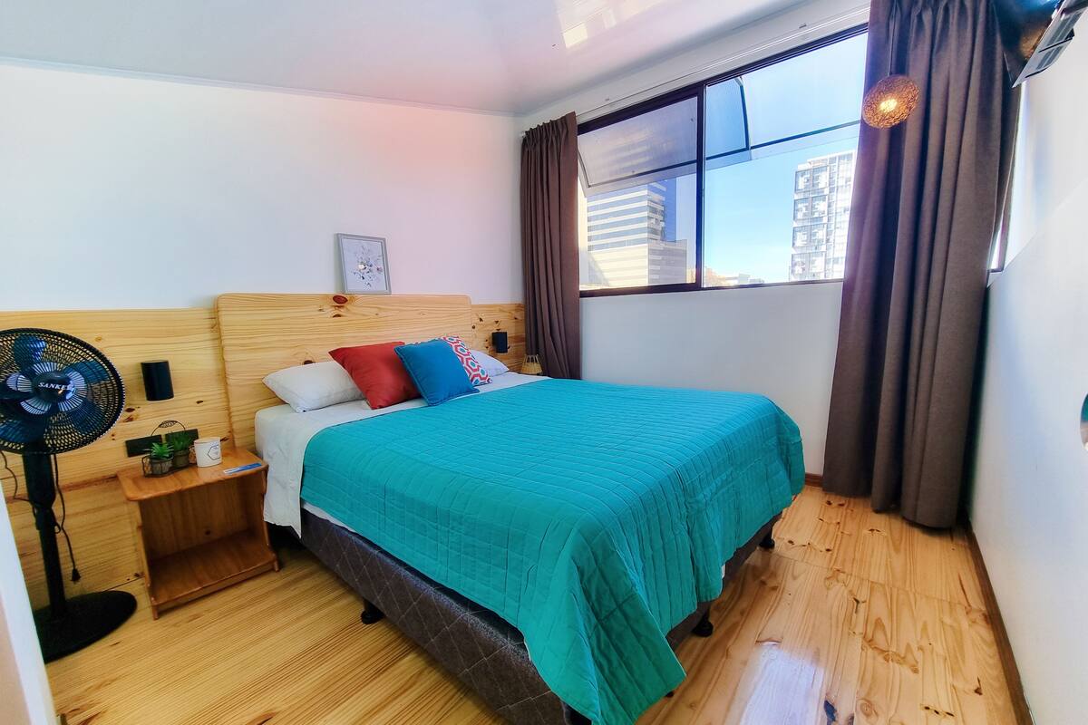A neatly arranged bedroom with a wooden headboard, a teal bedspread, and a nightstand with a fan.