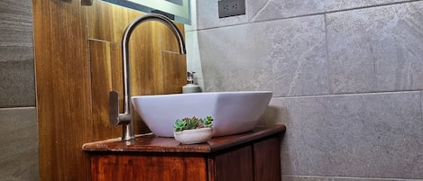 A bathroom with a wooden vanity, a white sink with a bowl, a small potted plant, and a toilet.