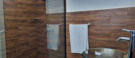 A modern bathroom with a glass shower enclosure, a glass sink, and wooden wall panels.