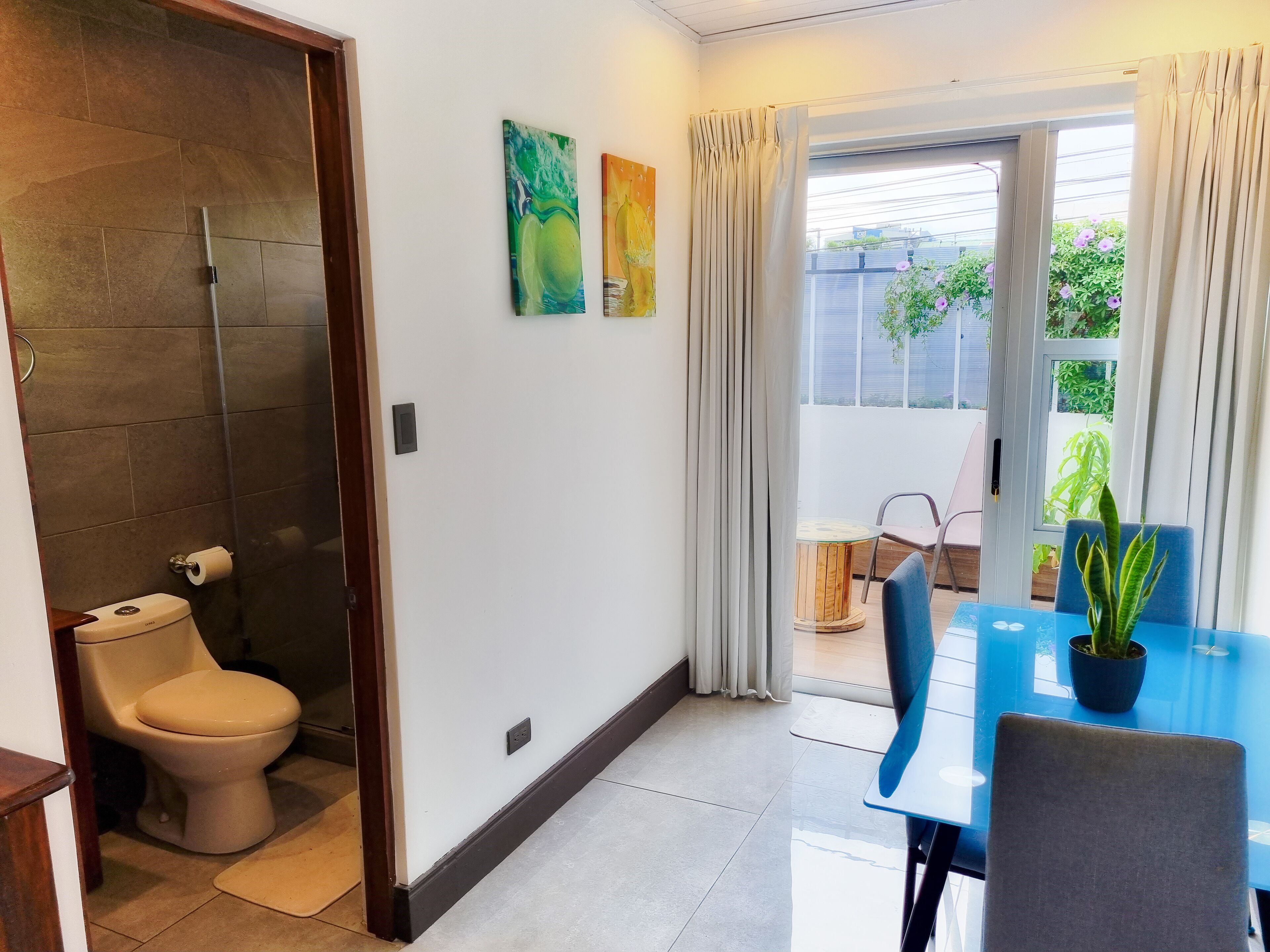 A modern bathroom with a toilet, shower, and a glass door leading to a balcony with a table and chairs.